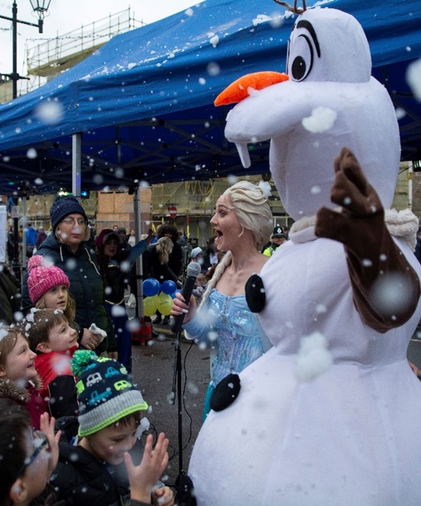 two people in fancy dress wave at children as fake snow falls around them all