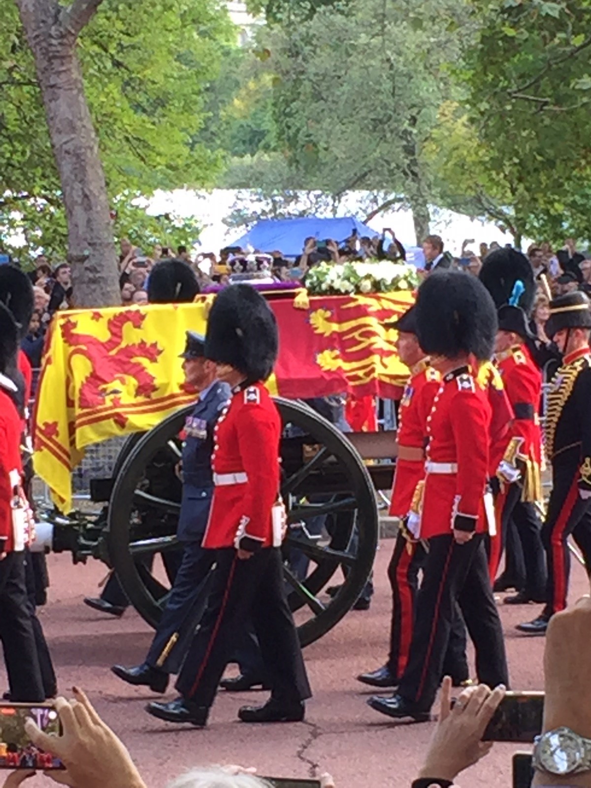 The queens coffin travels on top of a horse drawn cart with her Royal emblem draped over the top of the coffin, accompanied on both sides by various members of the armed forces. 